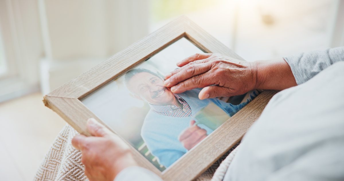 Person holding a framed photograph of a smiling loved one while reflecting on cherished memories.